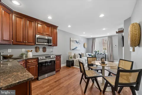 a open kitchen with stainless steel appliances granite countertop a stove top oven a sink dishwasher a dining table and chairs with wooden floor