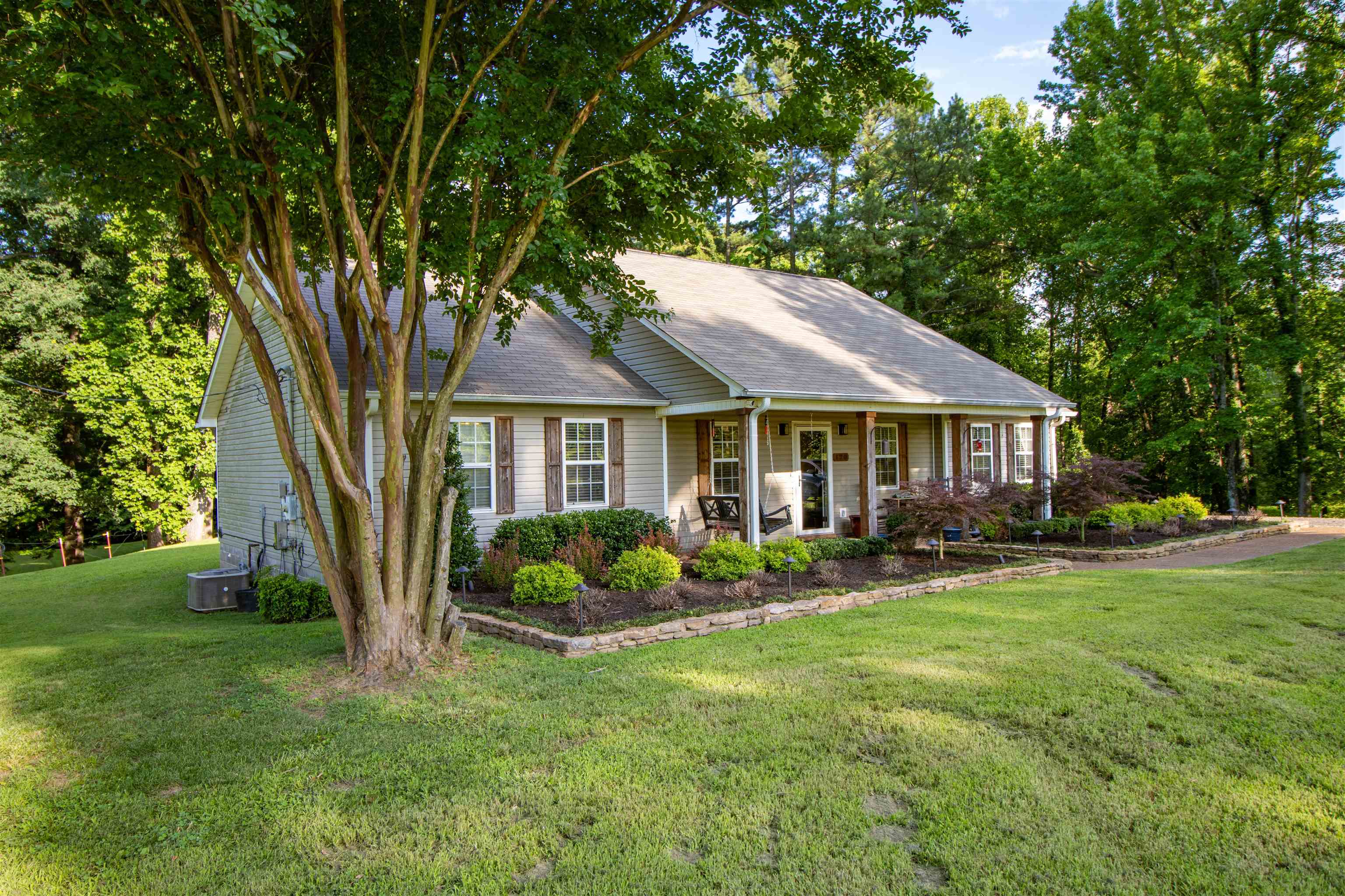 120 Craig Road Ripley, TN 38063 - Photo 37 of 38 Exterior featuring horizontal siding, a covered front porch with white columns, brown window shutters, a stone-lined garden bed with shrubs, and mature trees