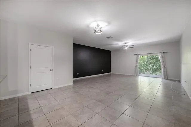 an empty room with chandelier fan and windows