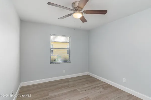 an empty room with wooden floor ceiling fan and windows