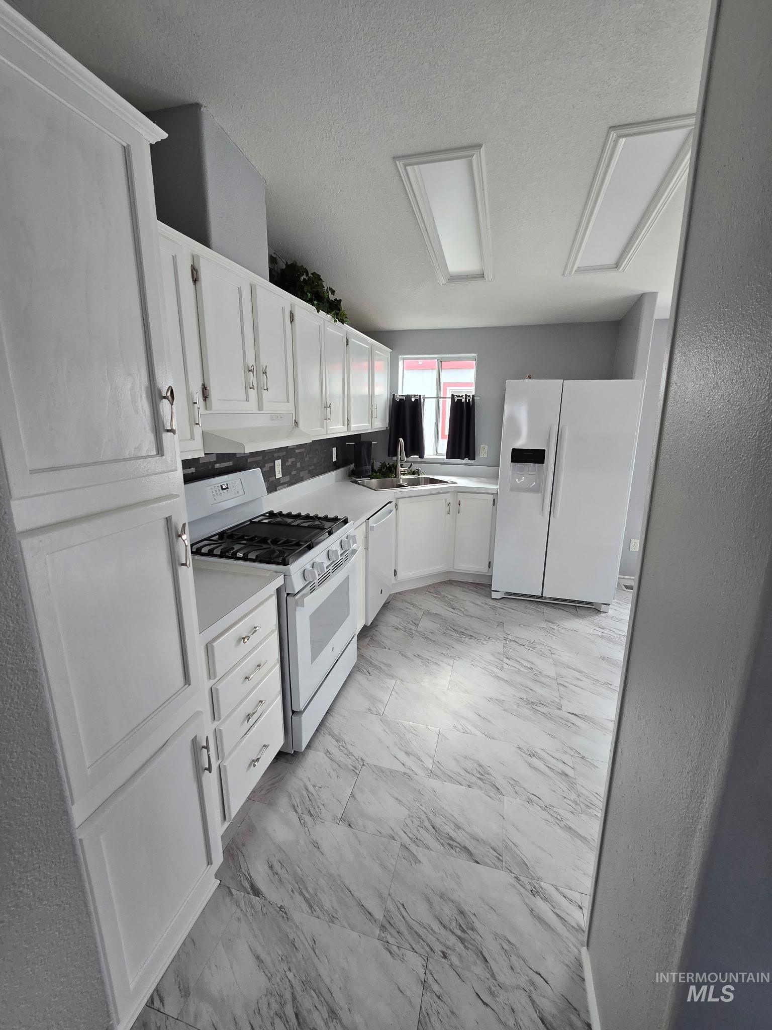 2115 6th Avenue, Unit 51 Clarkston, WA 99403 - Photo 25 of 34 Kitchen with white appliances, white cabinets, light marble finish floors, light countertops, and a textured ceiling