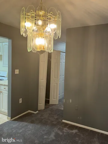 en empty room with a chandelier fan and kitchen view