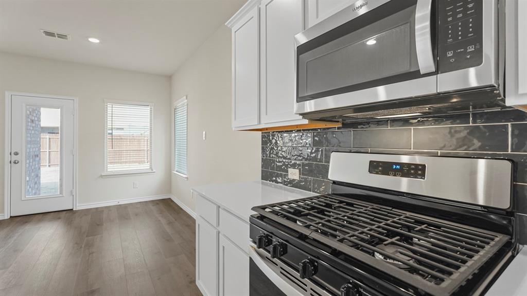 447 Epiphany Lane Lavon, TX 75166 - Photo 7 of 31 Modern kitchen featuring stainless steel appliances, crisp white cabinetry, a dark subway tile backsplash, light countertops, and wood-finish flooring
