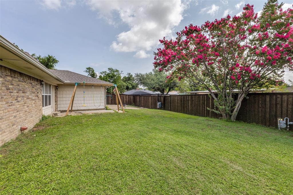 705 South Grove Road Richardson, TX 75081 - Photo 23 of 26 Spacious backyard featuring a manicured lawn, a mature flowering tree, and a robust privacy fence