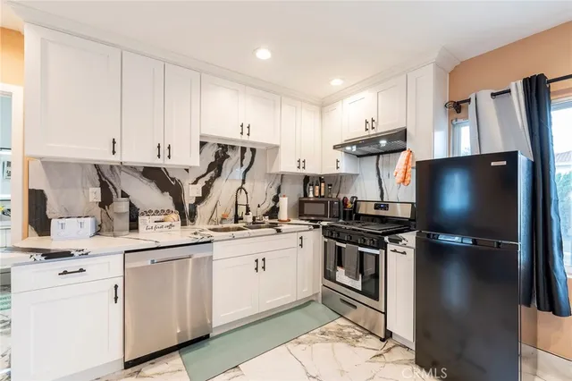 a kitchen with stainless steel appliances granite countertop a sink a stove a refrigerator and white cabinets
