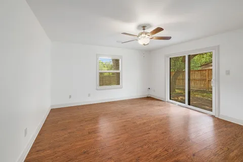 an empty room with wooden floor fan and windows