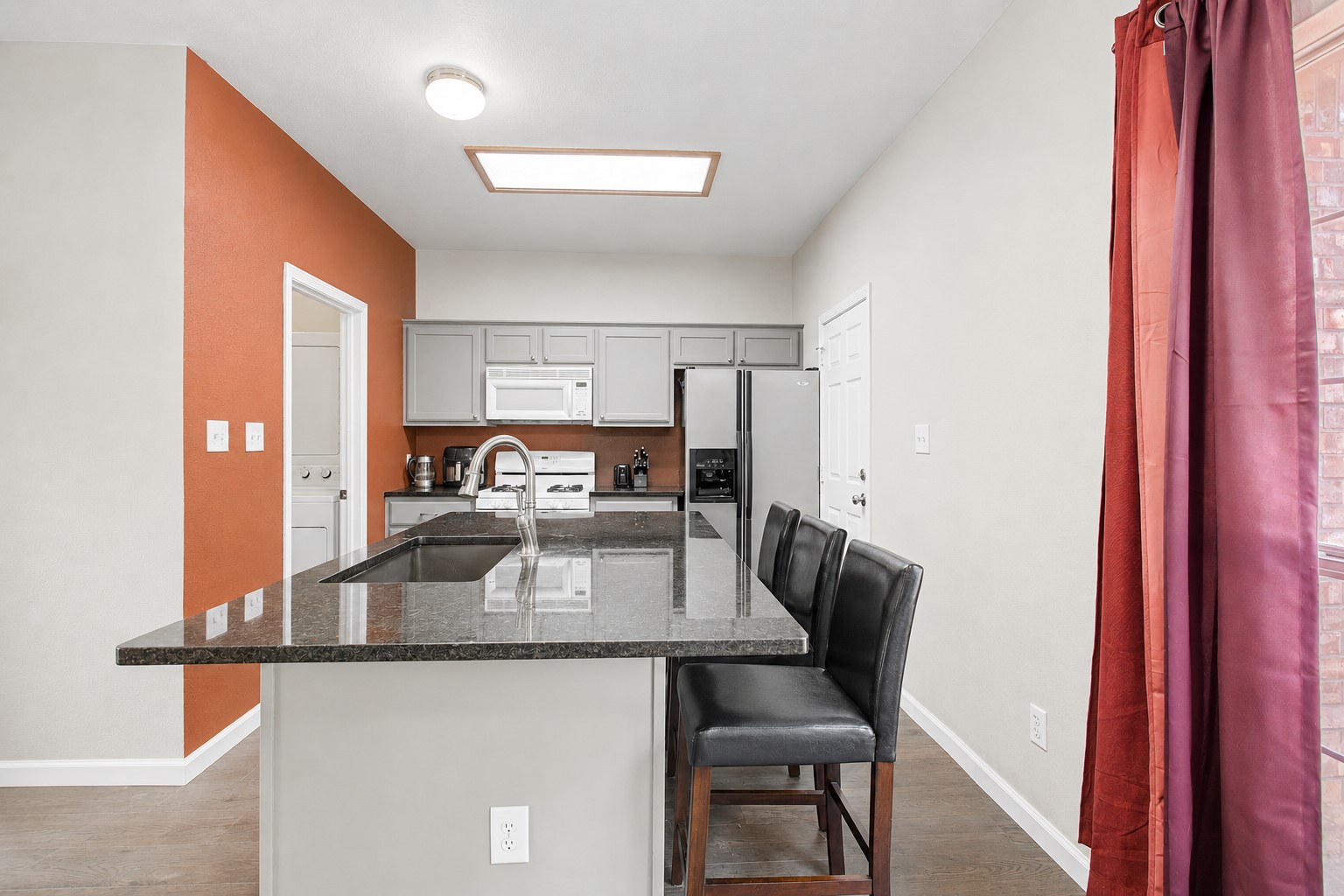 207 Kates Way Hutto, TX 78634 - Photo 14 of 24 Kitchen featuring an island with a built-in sink, gray cabinetry, stainless steel appliances, and wood-finish flooring.
Photo digitally edited to remove personal items.