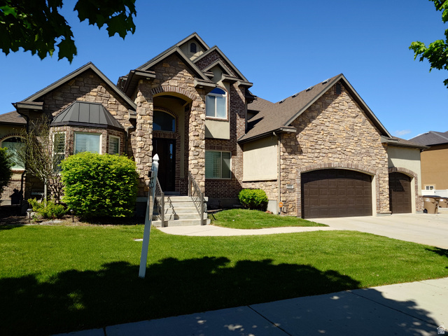 View of front of property featuring a front yard, a garage, concrete driveway, and stone siding