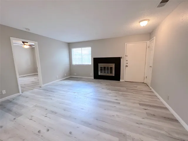 an empty room with wooden floor fireplace and windows