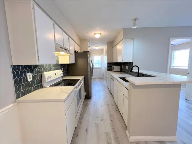 a large white kitchen with a stove a sink a refrigerator and a center island