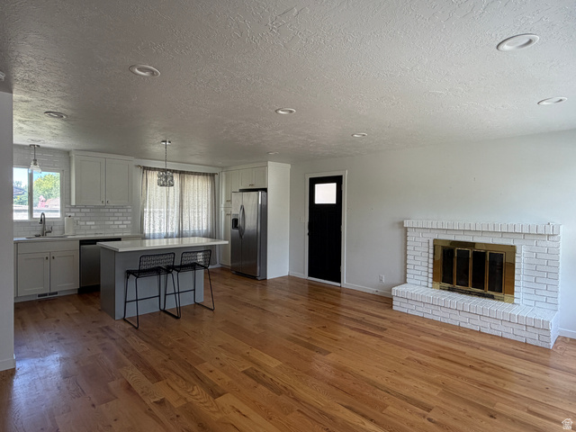 375 East 10560 South Sandy, UT 84070 - Photo 3 of 21 Open-concept living space featuring wood-finish flooring, a white brick fireplace with a brass firebox, and recessed ceiling lighting