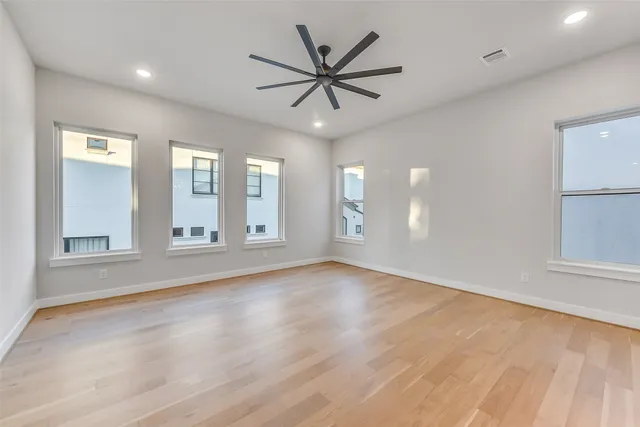 a view of an empty room with chandelier fan and wooden floor
