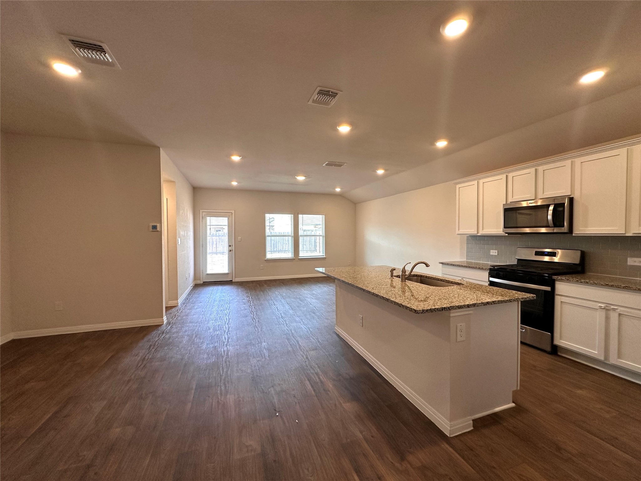 13804 Thomas Wheeler Way Manor, TX 78653 - Photo 26 of 27 Kitchen featuring stainless steel appliances, white cabinetry, a center island with sink, light stone counters, and open floor plan