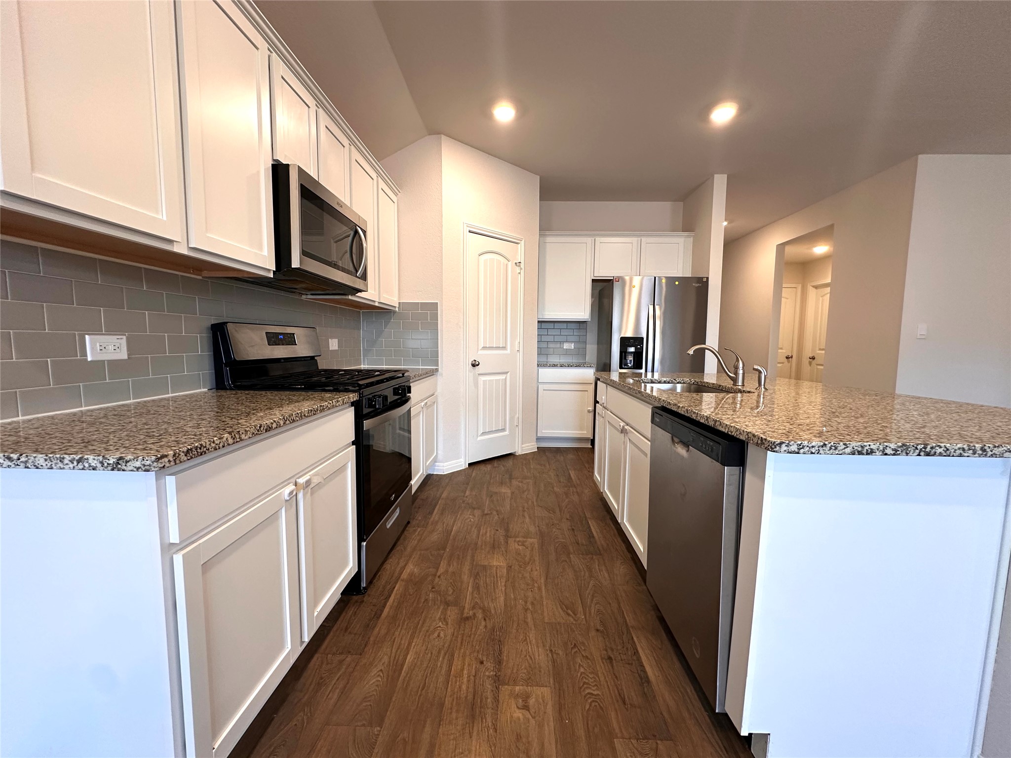 13804 Thomas Wheeler Way Manor, TX 78653 - Photo 13 of 27 Kitchen featuring stainless steel appliances, dark wood finished floors, white cabinetry, a kitchen island with sink, and recessed lighting