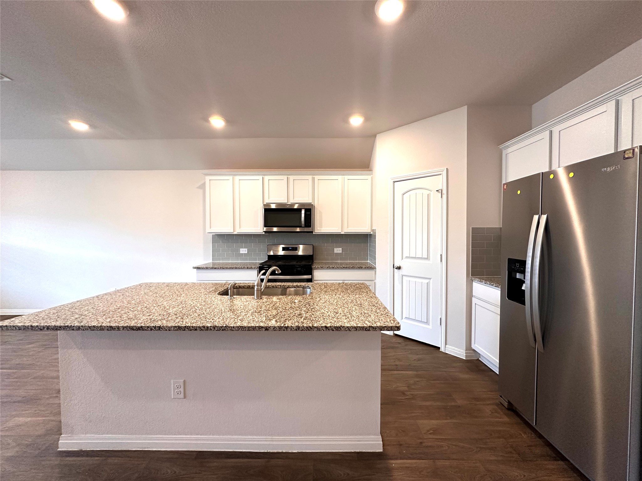 13804 Thomas Wheeler Way Manor, TX 78653 - Photo 14 of 27 Kitchen featuring stainless steel appliances, light stone countertops, white cabinetry, dark wood-type flooring, and an island with sink