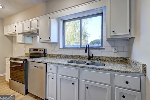 a kitchen with stainless steel appliances granite countertop white cabinets and a window