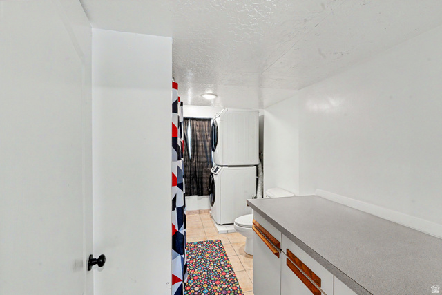 3689 Lasso Loop Circle Magna, UT 84044 - Photo 16 of 26 Laundry area featuring a stacked washer and dryer, tile flooring, and a built-in countertop with white cabinetry and wood-finish hardware