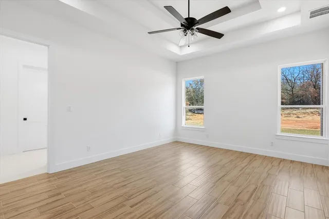 an empty room with wooden floor fan and windows
