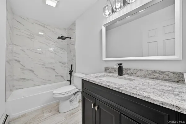 a bathroom with a granite countertop bathtub sink vanity mirror and toilet