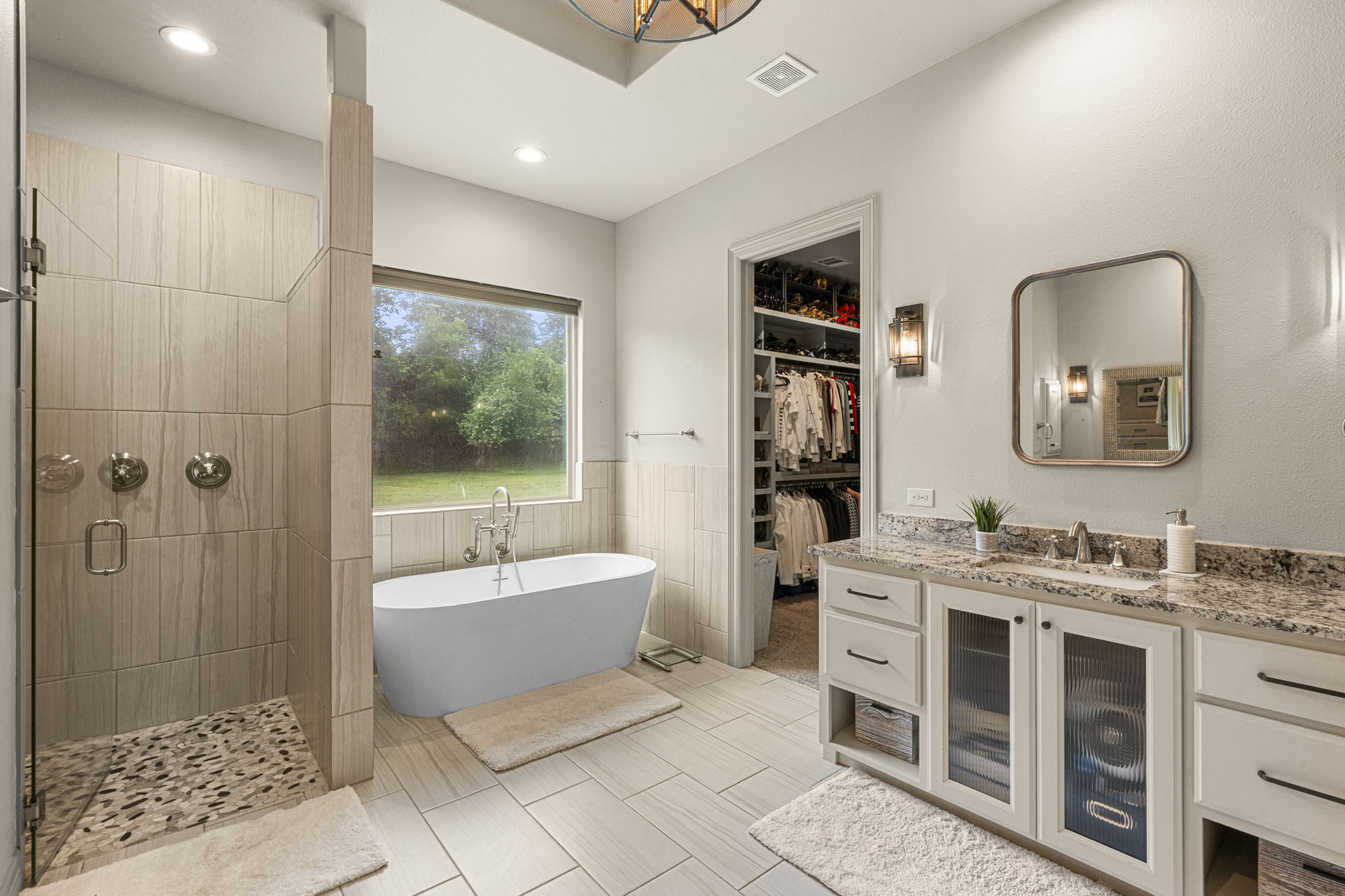 16202 Remuda Trail Buda, TX 78610 - Photo 14 of 40 Primary bathroom featuring a walk-in shower with a glass enclosure, a freestanding bathtub positioned by a large window, and a vanity with a granite countertop and ample storage