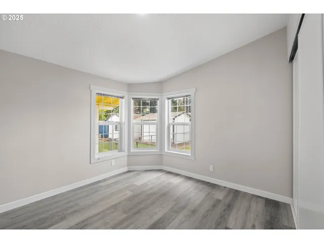 a view of an empty room with a window and wooden floor