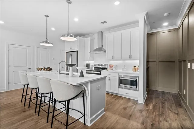 a kitchen with stainless steel appliances granite countertop a refrigerator a sink dishwasher a stove and white cabinets with wooden floor