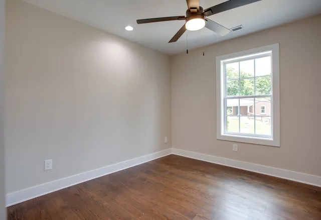 an empty room with wooden floor ceiling fan and windows