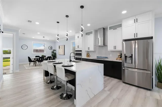 a kitchen with stainless steel appliances kitchen island granite countertop a refrigerator a stove a sink a dining table and chairs with wooden floor
