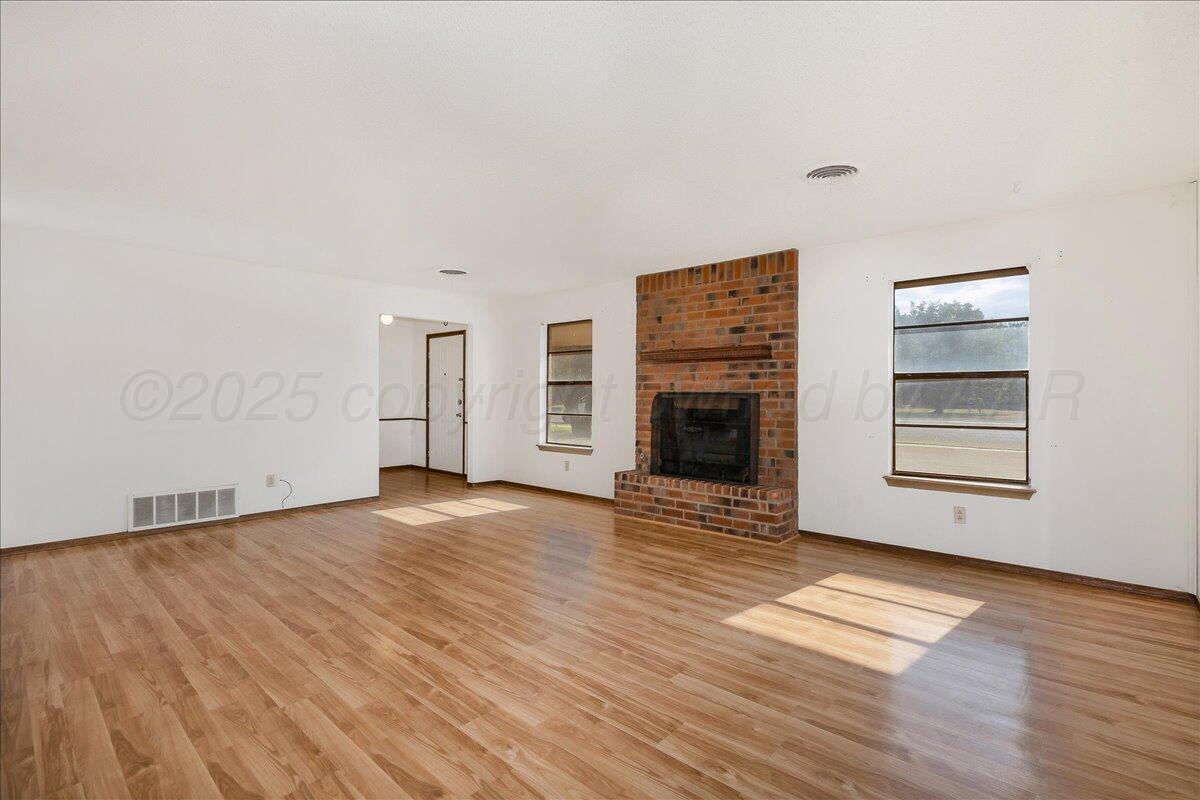 7210 Hatton Road Amarillo, TX 79110 - Photo 4 of 23 an empty room with wooden floor fireplace and windows