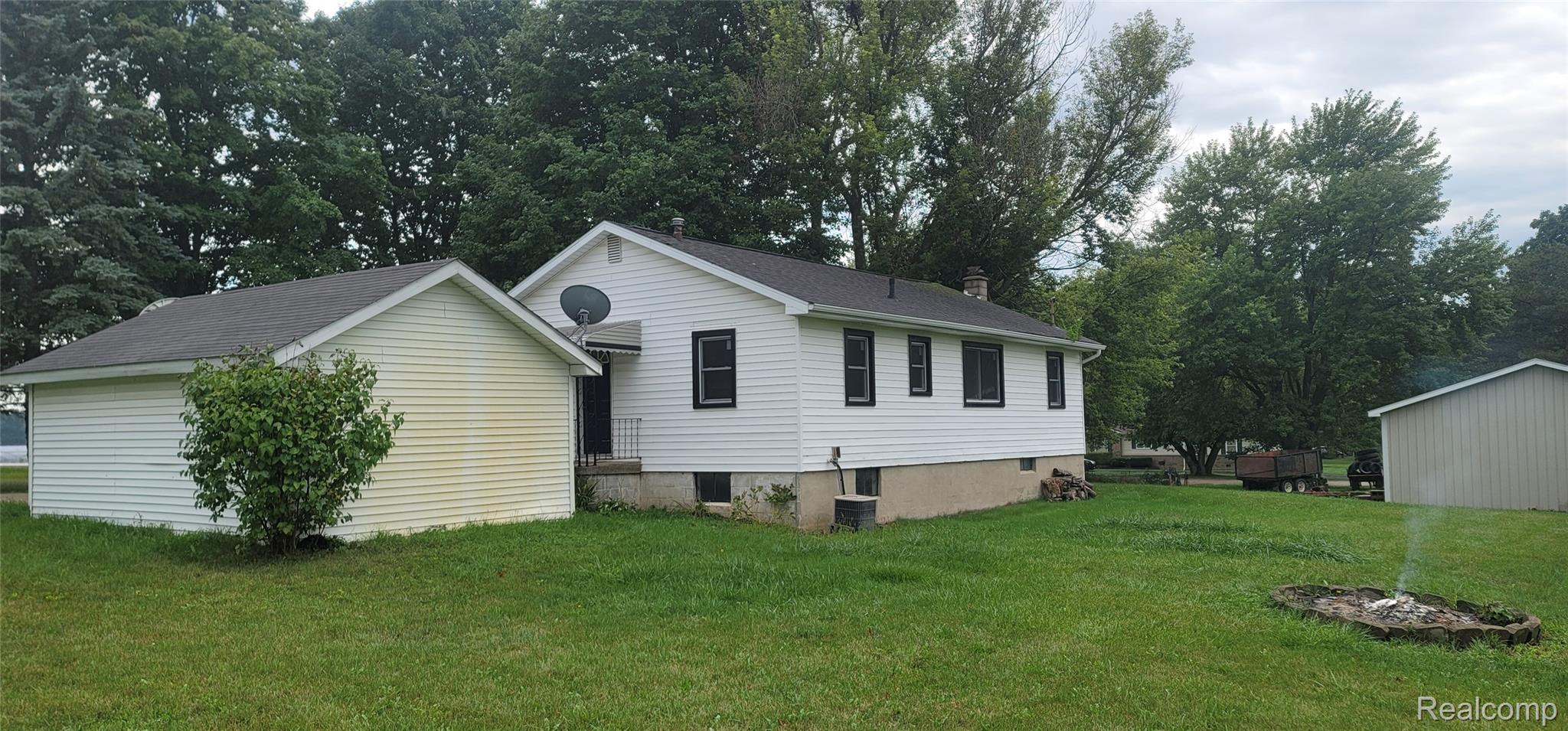 White siding exterior with black window frames, an attached outbuilding, a detached shed, and a fire pit