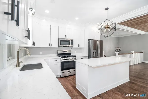 a kitchen with stainless steel appliances a stove a sink dishwasher a refrigerator white cabinets and wooden floor