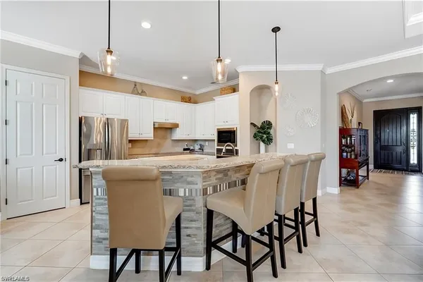 a kitchen with stainless steel appliances kitchen island granite countertop a dining table chairs and a refrigerator