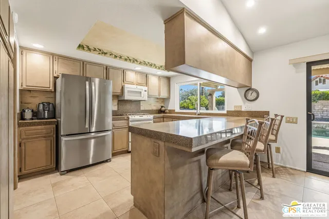 a kitchen with stainless steel appliances granite countertop a refrigerator a sink a stove and a dining table with wooden floor