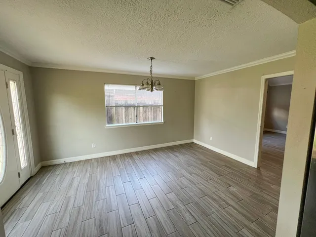 an empty room with wooden floor chandelier and windows