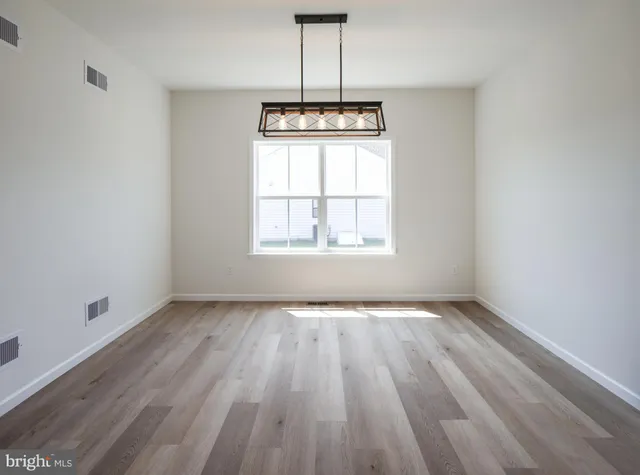 an empty room with wooden floor chandelier and windows
