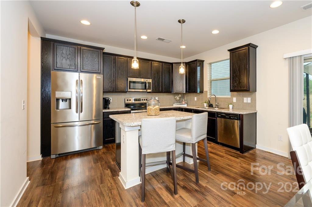 4626 Gibbons Link Road Charlotte, NC 28269 - Photo 5 of 20 a kitchen with stainless steel appliances kitchen island granite countertop a refrigerator a stove a sink a dining table and chairs with wooden floor