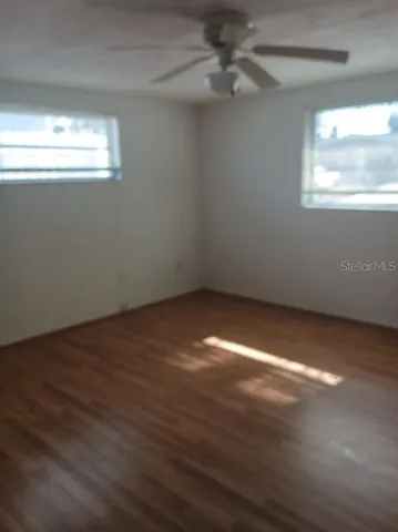 an empty room with wooden floor chandelier fan and windows