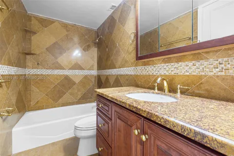 a bathroom with a granite countertop bathtub sink vanity mirror and toilet