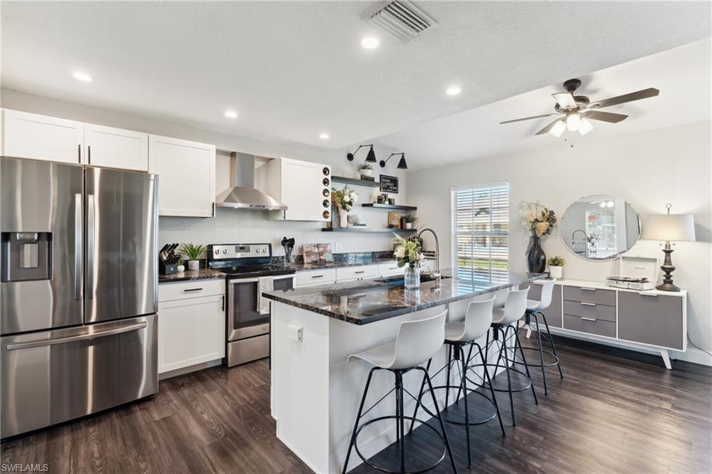 8457 Wren Road Fort Myers, FL 33967 - Photo 23 of 50 Kitchen featuring white cabinets, wall chimney range hood, a kitchen island with sink, and appliances with stainless steel finishes