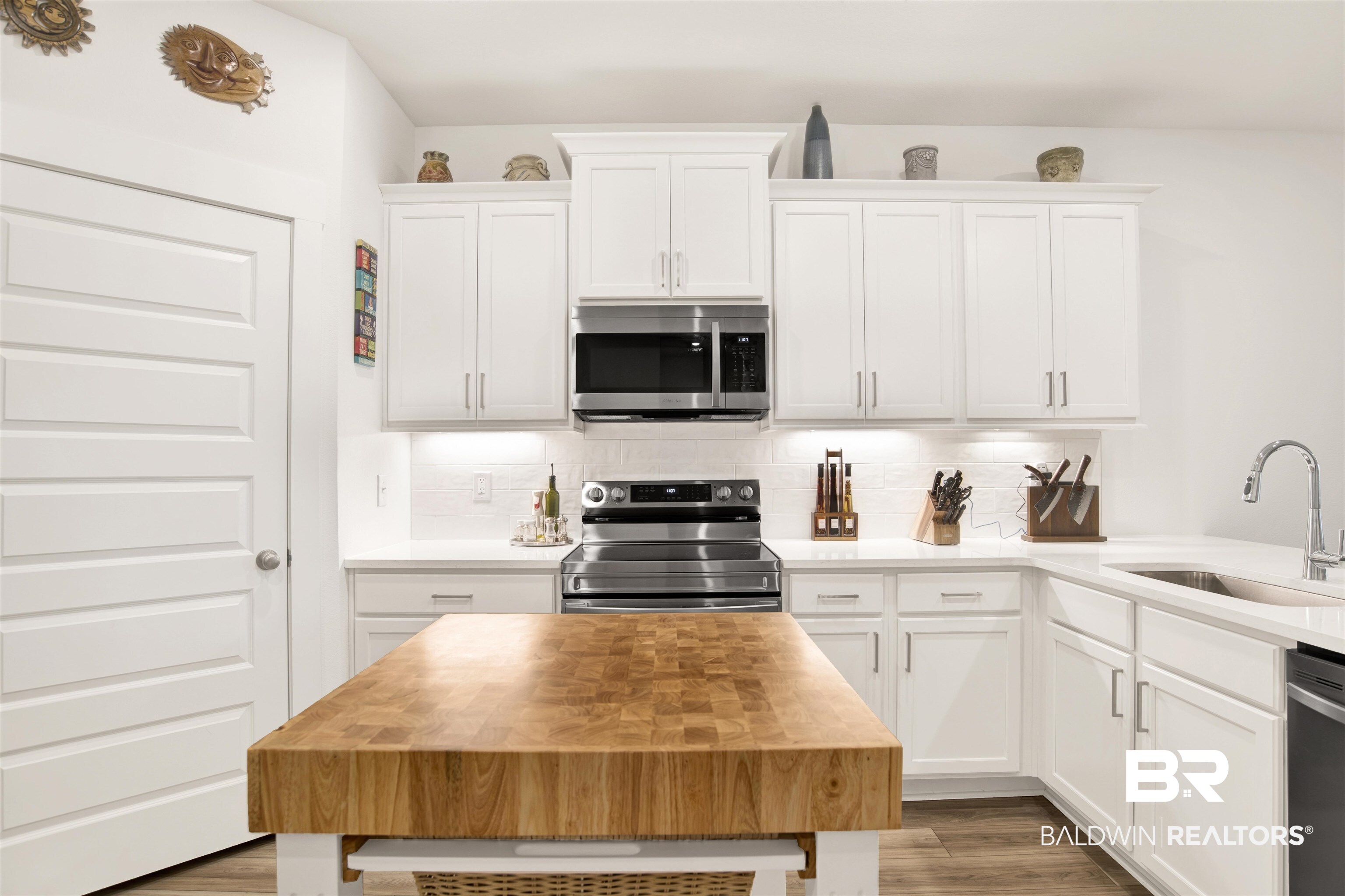 Kitchen with stainless steel appliances, backsplash, white cabinets, and wood finished floors