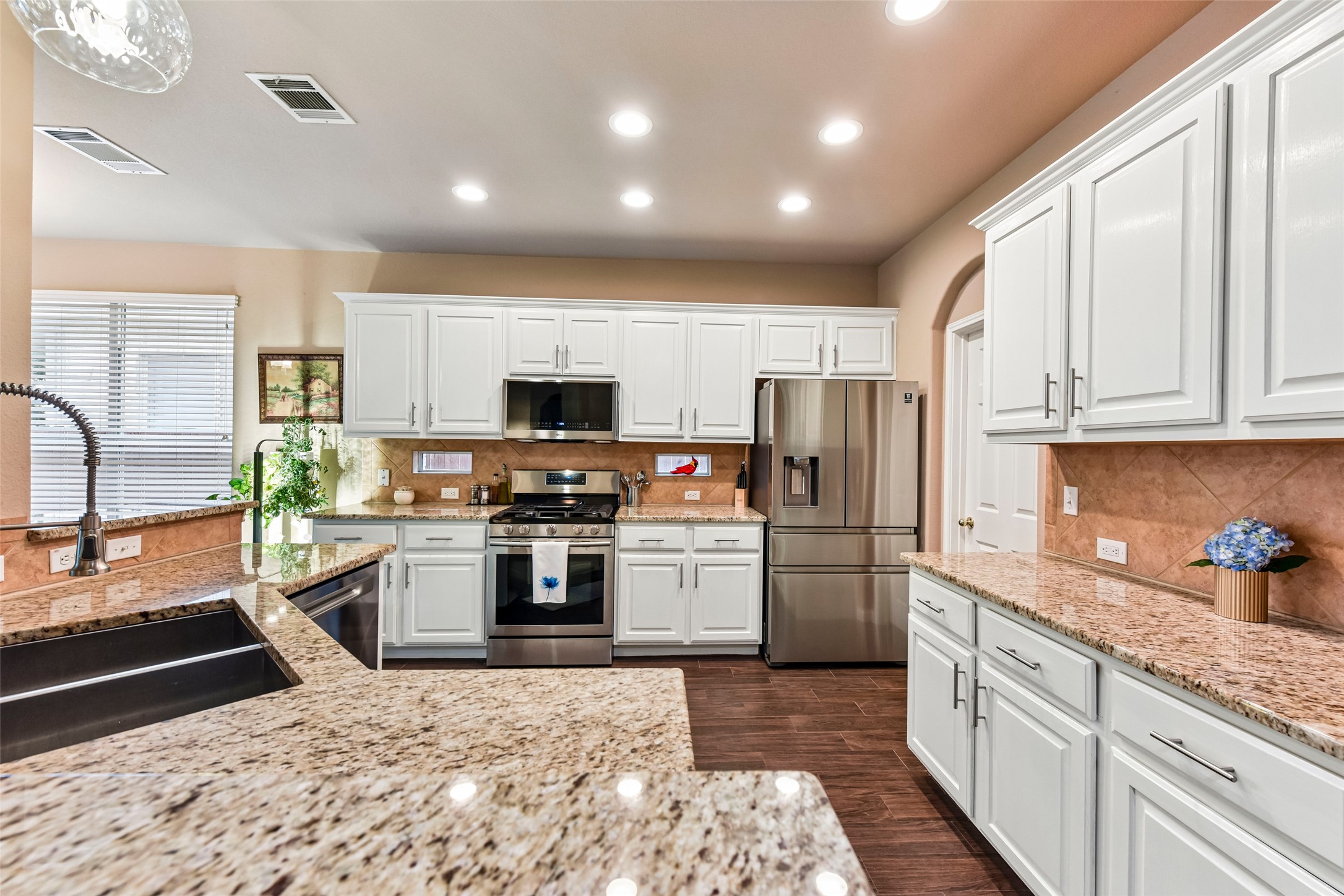 10216 Anahuac Trail Austin, TX 78747 - Photo 18 of 39 a kitchen with kitchen island granite countertop a refrigerator oven a sink dishwasher and white cabinets with wooden floor