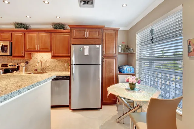 a kitchen with stainless steel appliances granite countertop a refrigerator a sink a stove a dining table and chairs