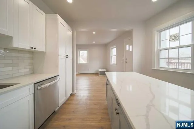 a large white kitchen with kitchen island a sink wooden floor and stainless steel appliances