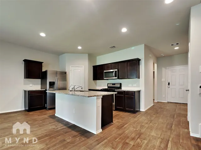 a kitchen with stainless steel appliances a stove top oven a sink dishwasher a refrigerator and a oven with wooden floor