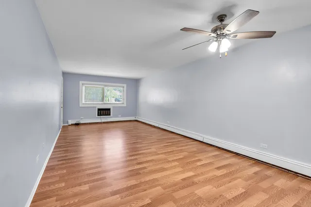 an empty room with wooden floor chandelier fan and windows