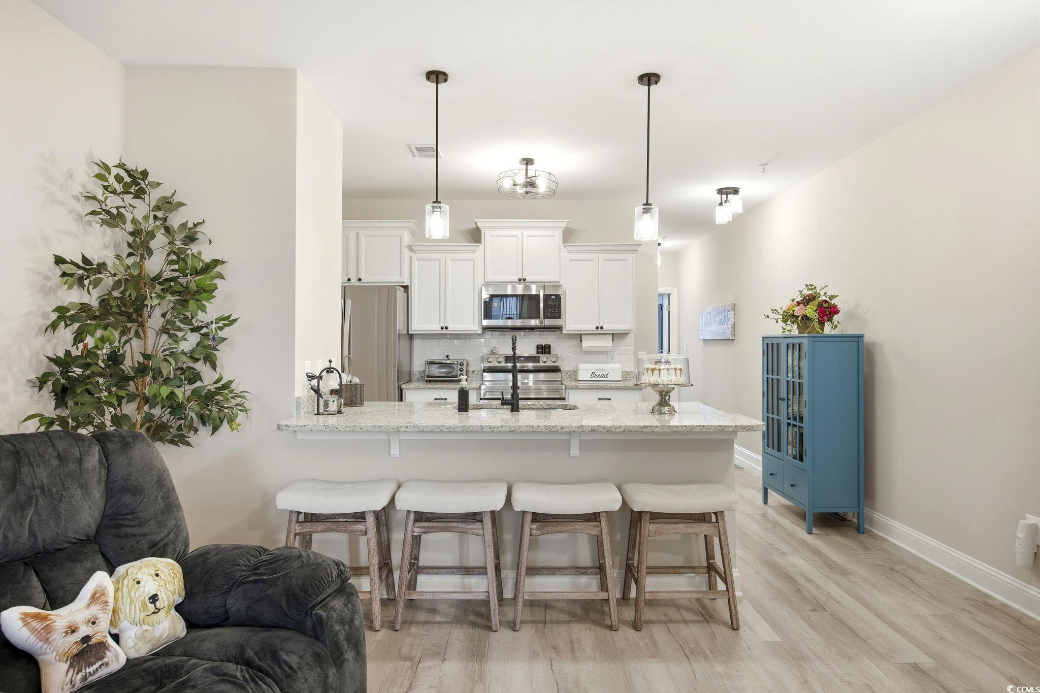 165 Ella Kinley Circle, Unit 302 Myrtle Beach, SC 29588 - Photo 11 of 38 Kitchen with a breakfast bar area, white cabinetry, a peninsula, tasteful backsplash, and light stone counters