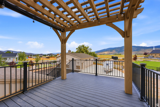 560 Aspen Road Francis, UT 84036 - Photo 10 of 59 Expansive composite deck with wood-finish flooring and overhead pergola structure, featuring black metal railings and sweeping vistas of rolling hills and mountain landscape beyond neighboring properties