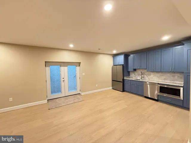 a view of an empty room with kitchen and window