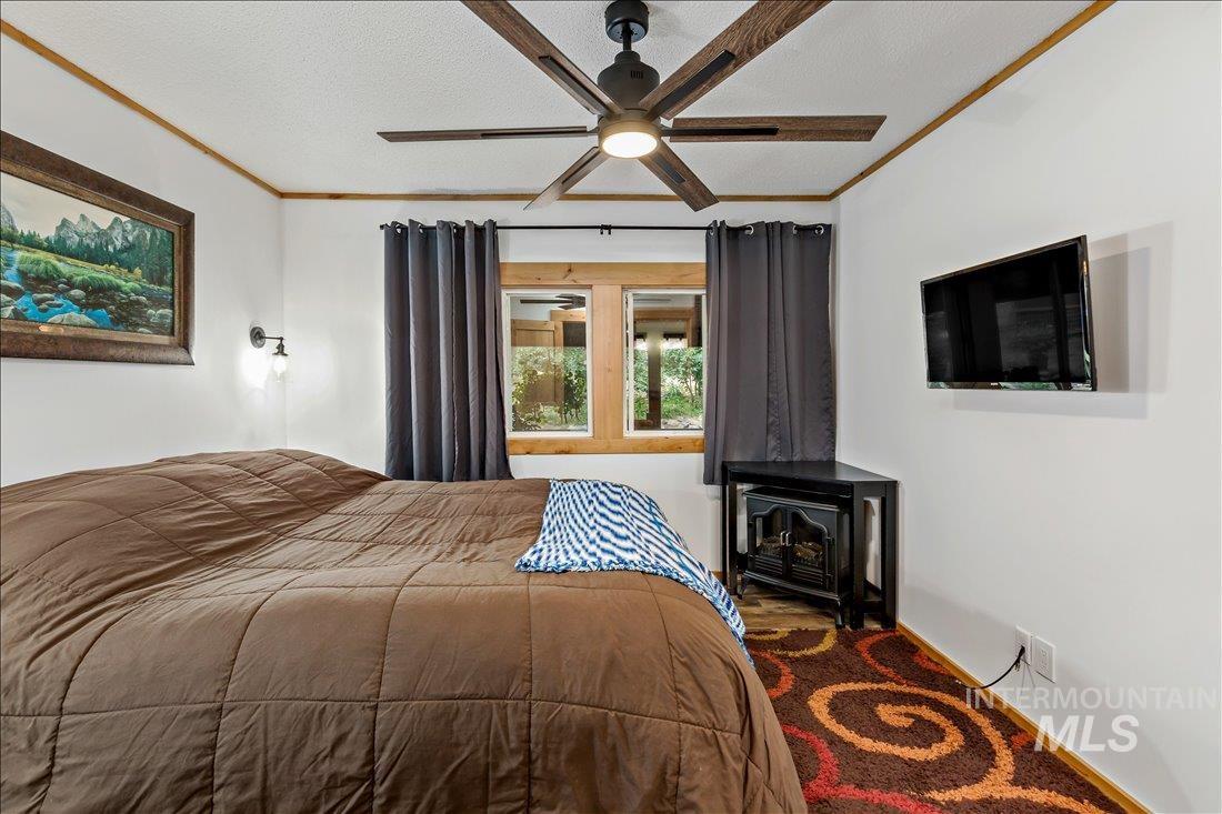 79 Sunset Loop Cascade, ID 83611 - Photo 20 of 44 Bedroom featuring a ceiling fan with wood-finish blades, a wall-mounted television, and a corner electric fireplace unit