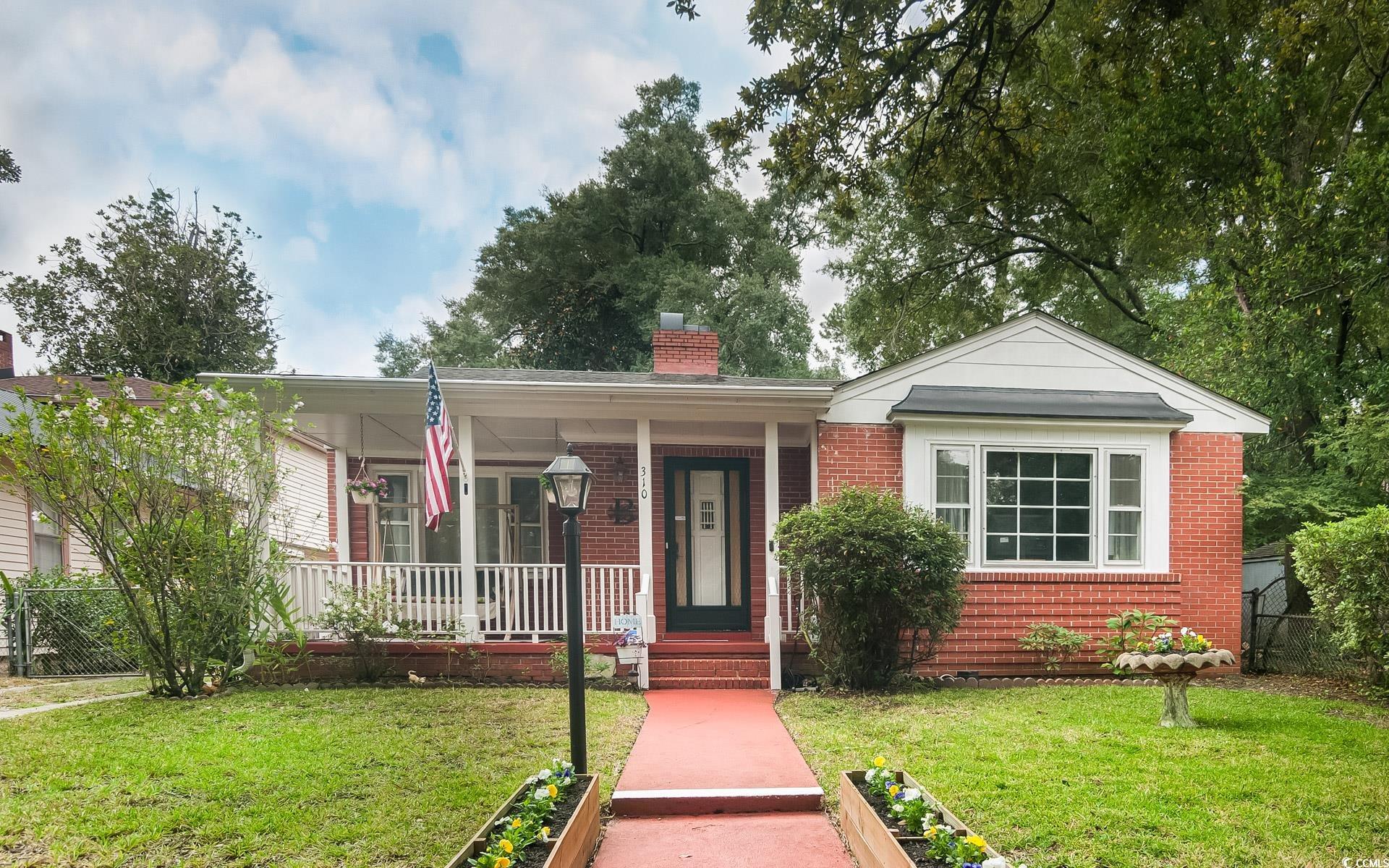 View of front facade with brick siding, a chimney, and covered porch